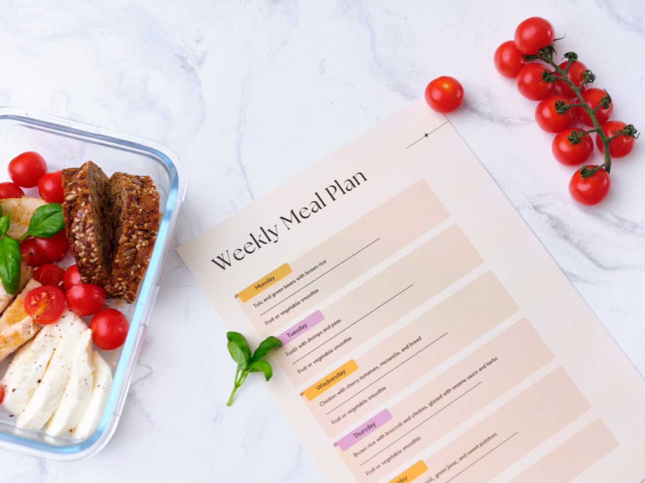 A weekly meal plan next to a prepped lunch of chicken, mozzarella and tomatoes